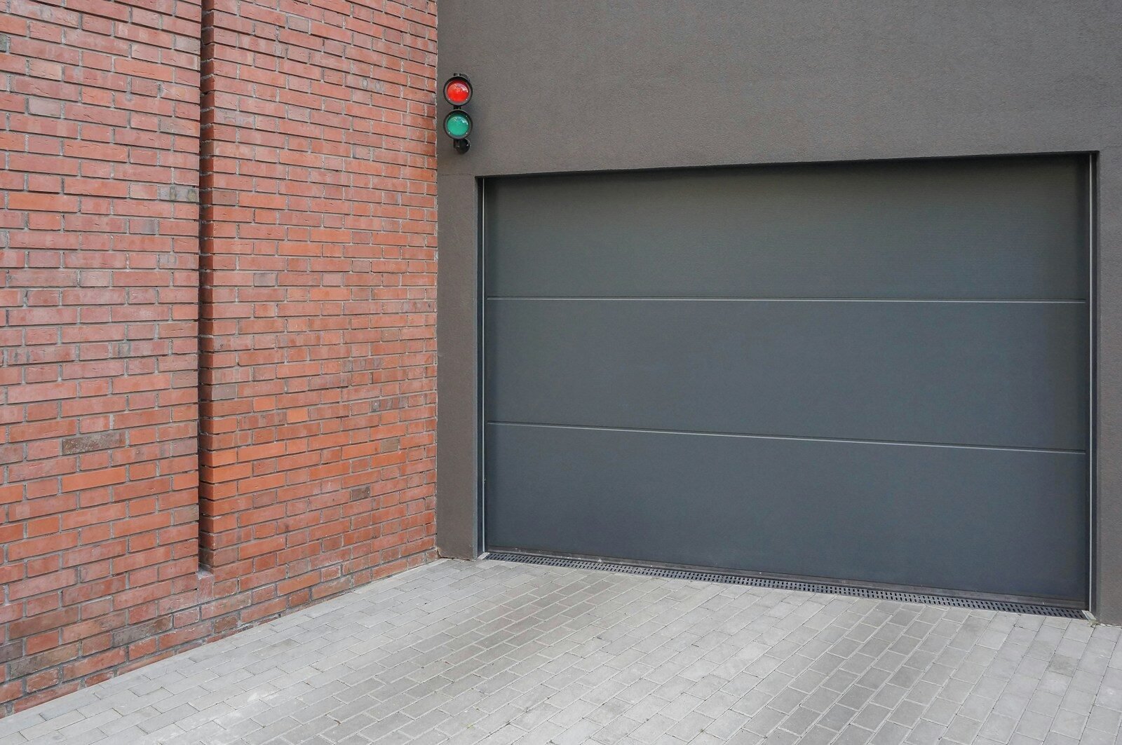 A grey garage door next to a brick wall